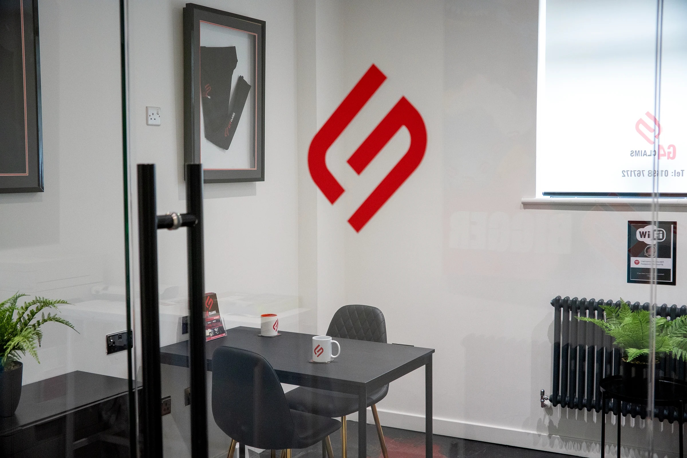 The meeting room at G4 Claims HQ in Wishaw, seen through the glass door, with the red G4 logo on the wall and a table with two G4 mugs